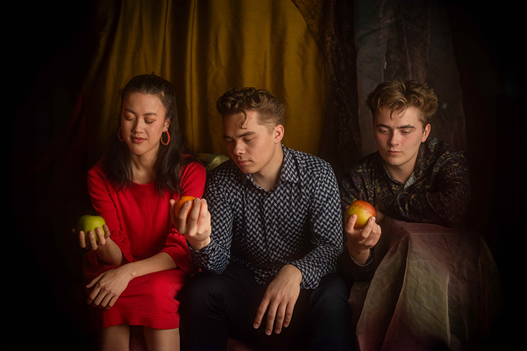 Kuvassa on kolme nuorta Radalla-festivaalin muusikkoa. Jokainen heistä katsoo kädessään olevaa omenaa. Kuva...