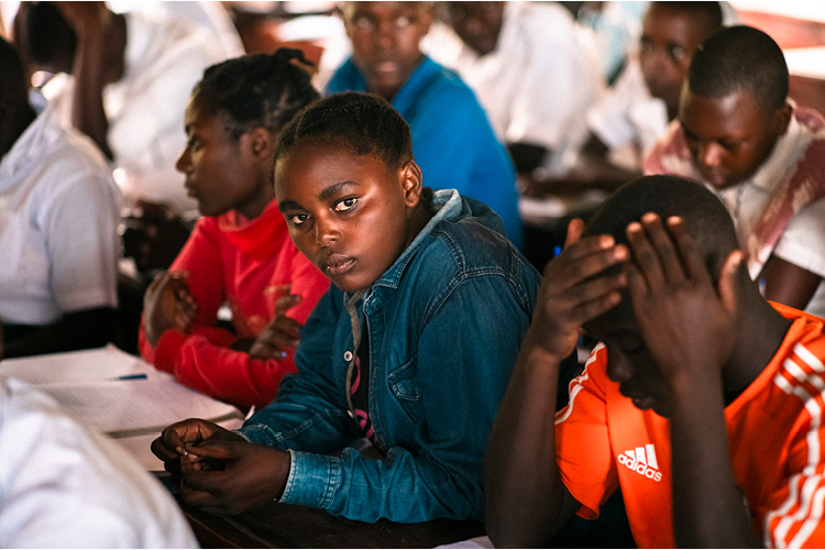 Ugandalaiset pakolaisnuoret koulussa. Tyttö keskellä katsoo kameraan.