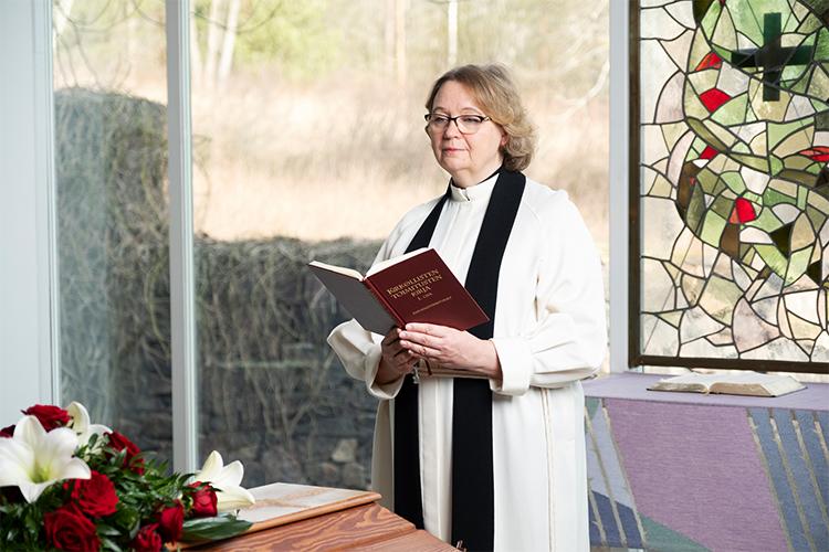 Kuvituskuvassa naispuolinen pappi seisoo arkun päädyssä kappelissa.