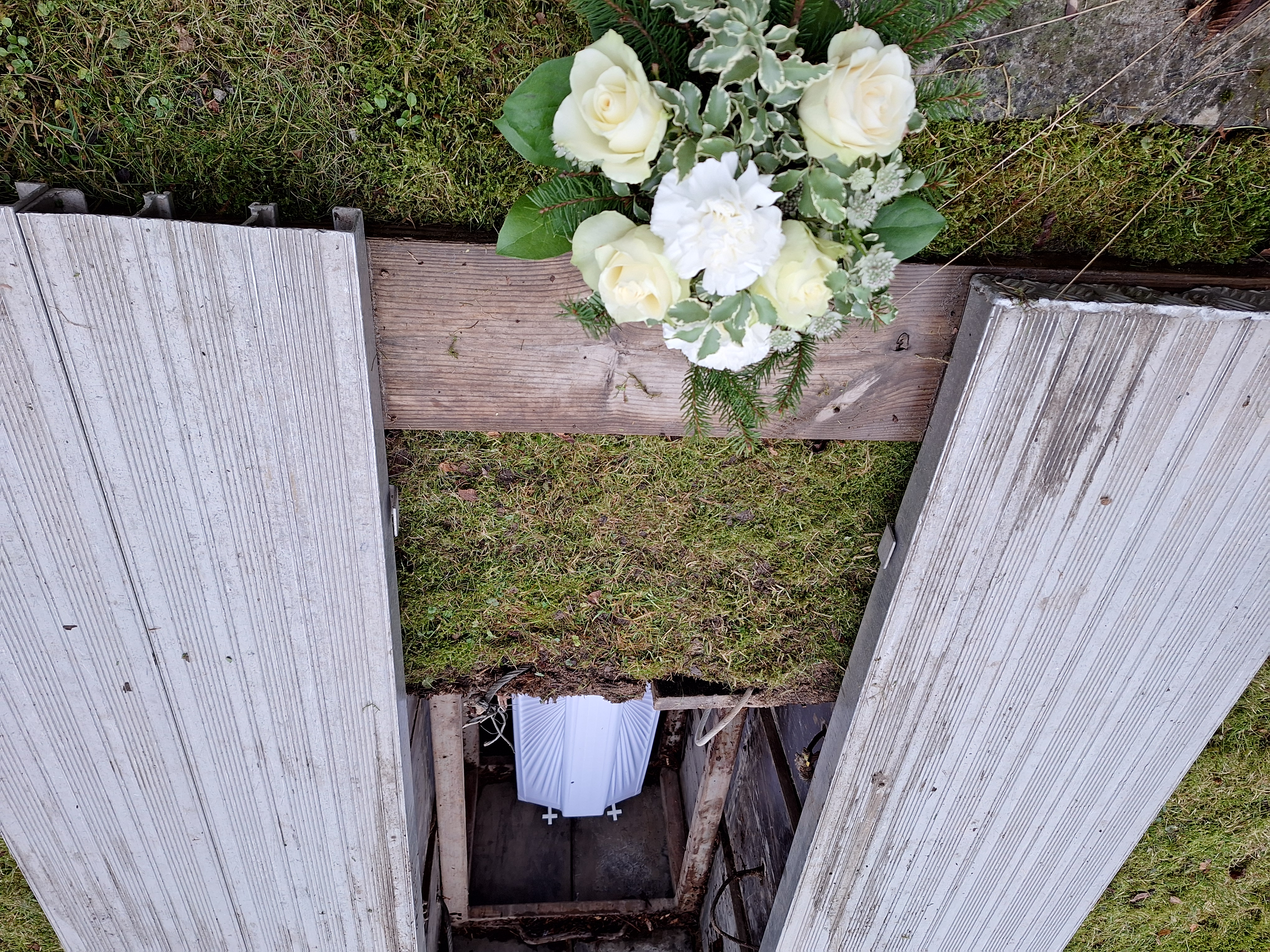 Kuvassa on avoin hauta, sen päädyssä kukkakimppu.