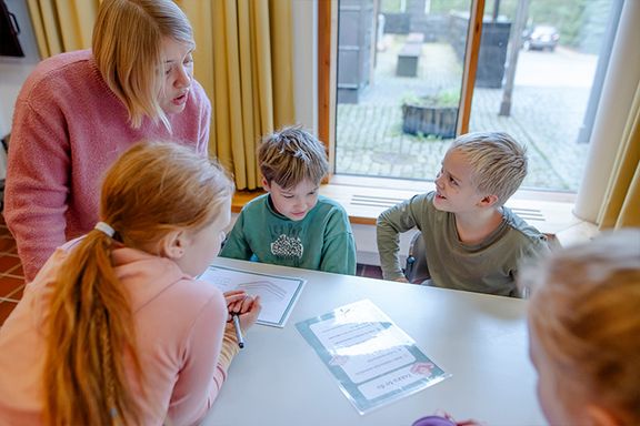 Neljäsluokkalaiset tekevät ryhmätyötä pöydän ääressä leirikeskuspäivässä opettajan johdolla.