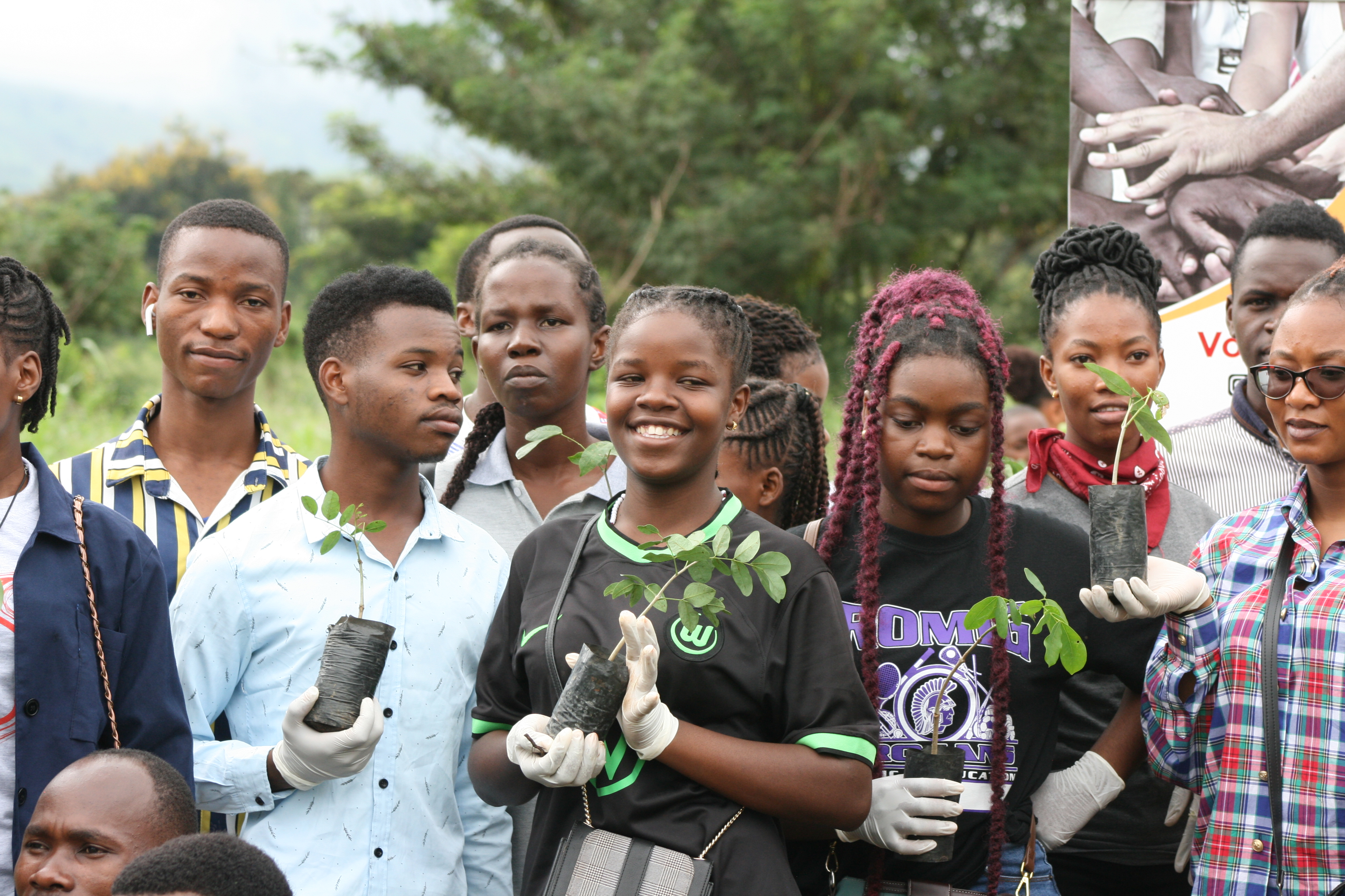 A group of young people is standing with small tree plants in their hands.