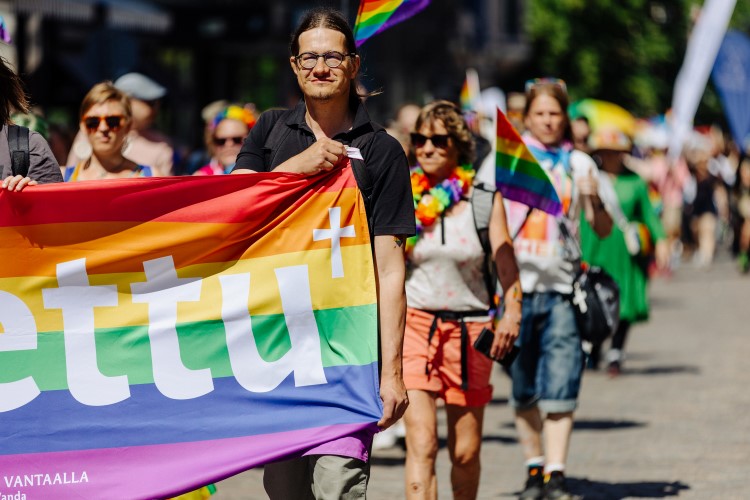 A group of people walk along a street. They are celebrating pride and diversity. In the foreground a man ho...