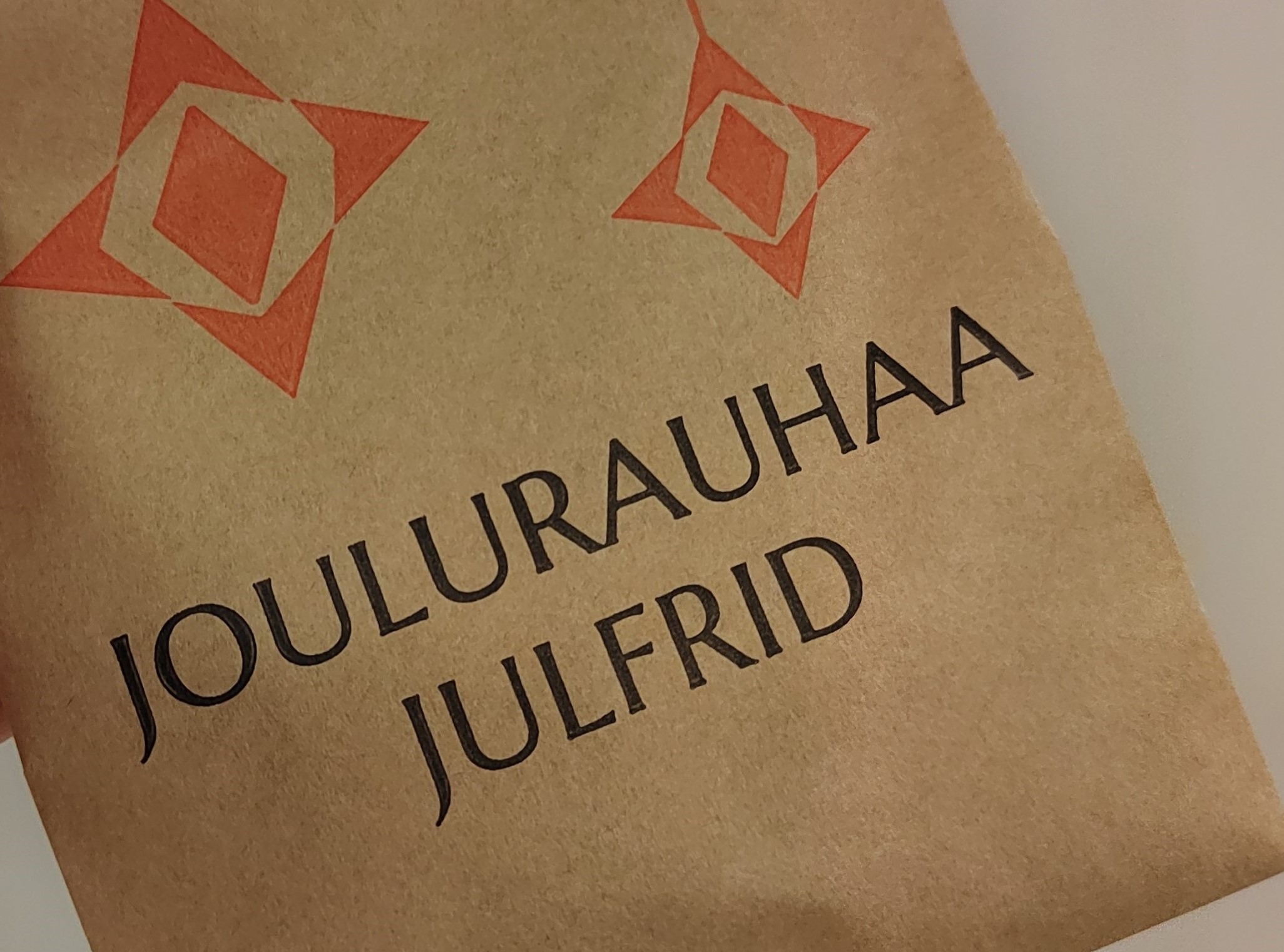 Joulurauhaa & Julfrid -tekstit ruskean paperipussin päällä. Pussissa piirrettynä punaisia joulukoristeita.