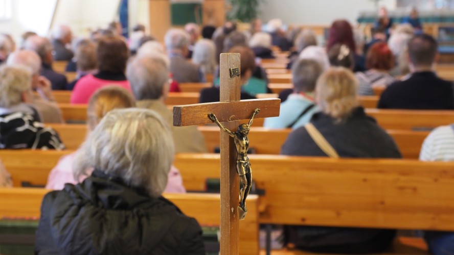Etualalla krusifiksi, taustalla ihmisiä kirkossa istumassa.