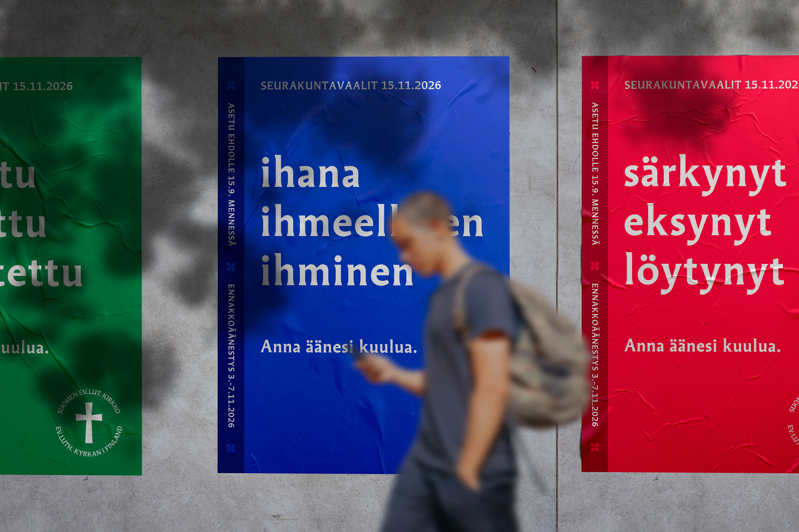 Kolme julistetta eri väreissä, joissa on tekstejä. Taustalla kävelee henkilö, joka on epätarkka.