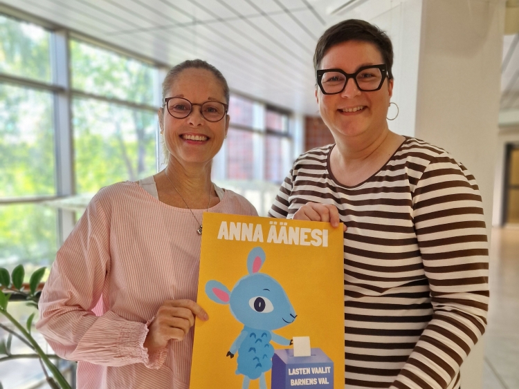 Tiina Hänninen ja Mirja Miettinen käsissään Lastenvaalien juliste, jossa on Lastenkirkon piirroshahmo Päkä-...