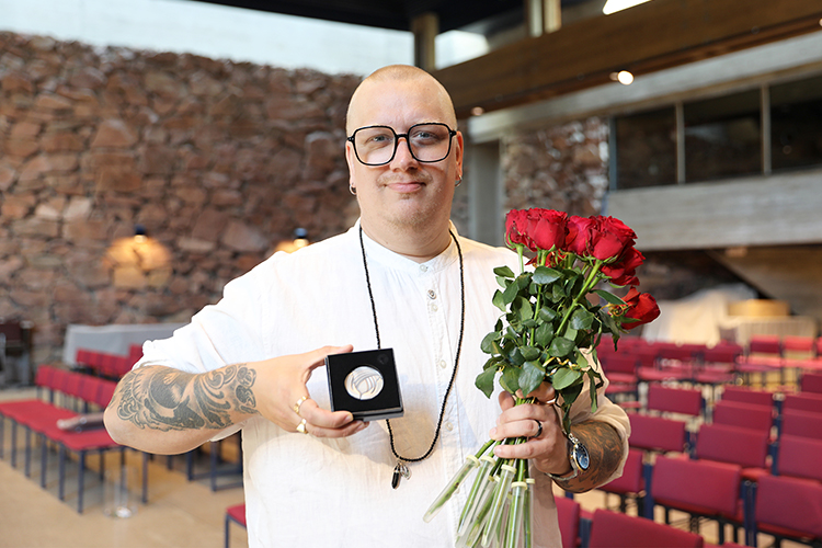 Kuvassa on Arttu Wiskari. Hänellä on käsissään Pro diaconia -mitali ja kimppu punaisia ruusuja.