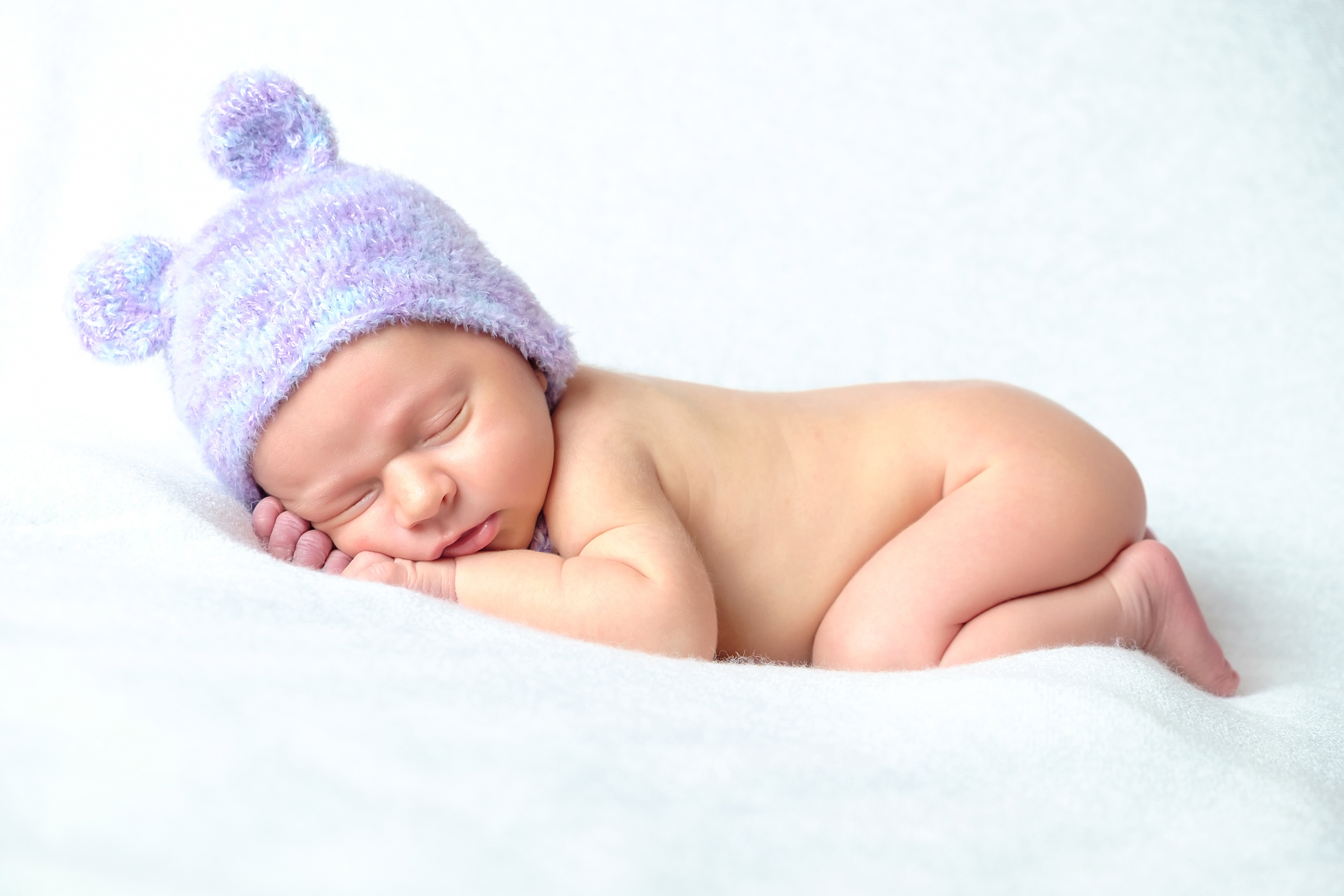 Kuvassa vastasyntynyt vauva nukkuu mahallaan violetti hattupäässä.