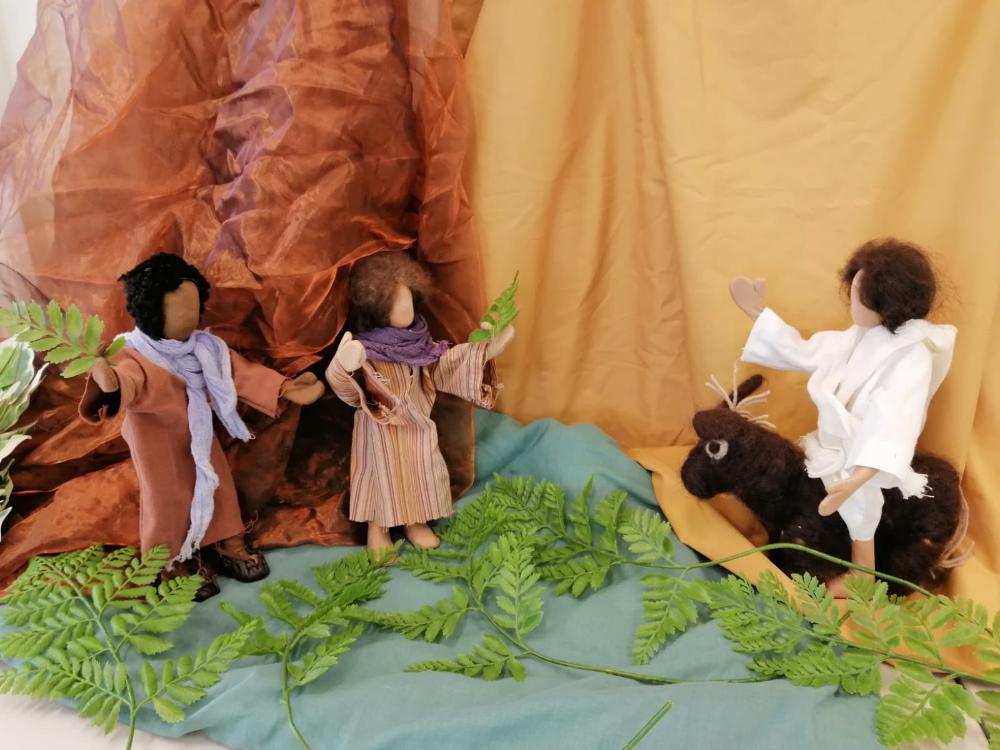 Nukke-Jeesus ratsastaa aasilla ja nukkeihmiset heiluttavat palmunoksia.