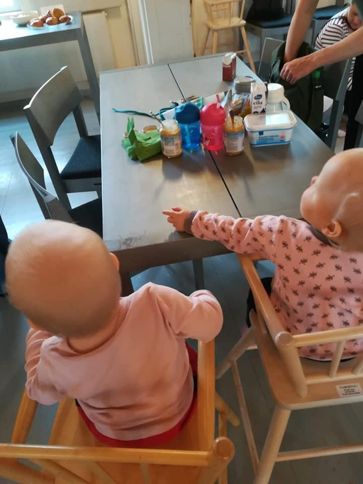 Kaksi vauvaa syöttötuolissa pöydän ääressä.