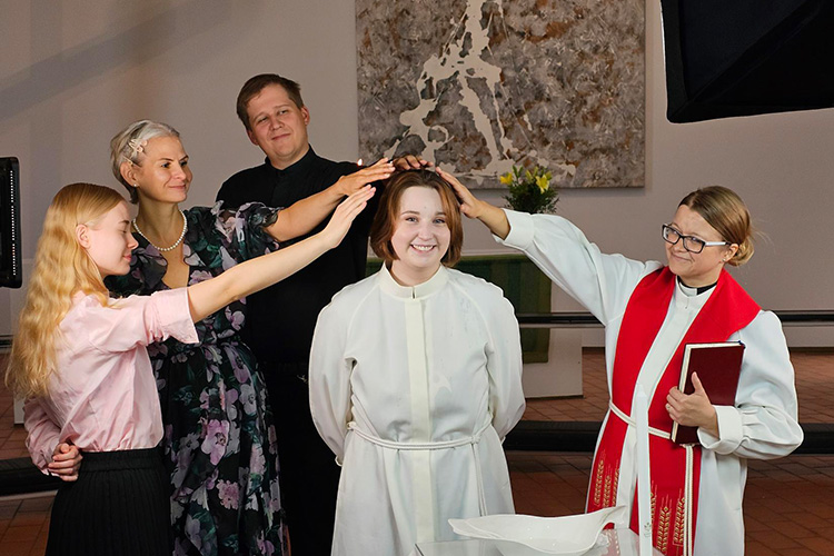 läheiset, kummit ja pappi siunaavat nuorta kastettavaa pitämällä käsiä hänen päänsä yllä