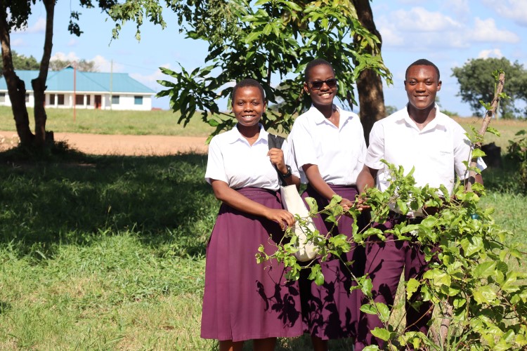 Three secondary school pupils by a passion fruit tree, with a low building in the background. 