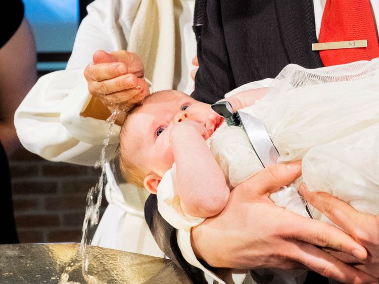 Pappi valelee vauvan päähän vettä kastemaljasta.