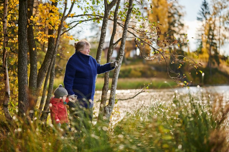 Vanhus ja lapsi kävelevät rannalla käsi kädessä. Maisema on syksyinen.