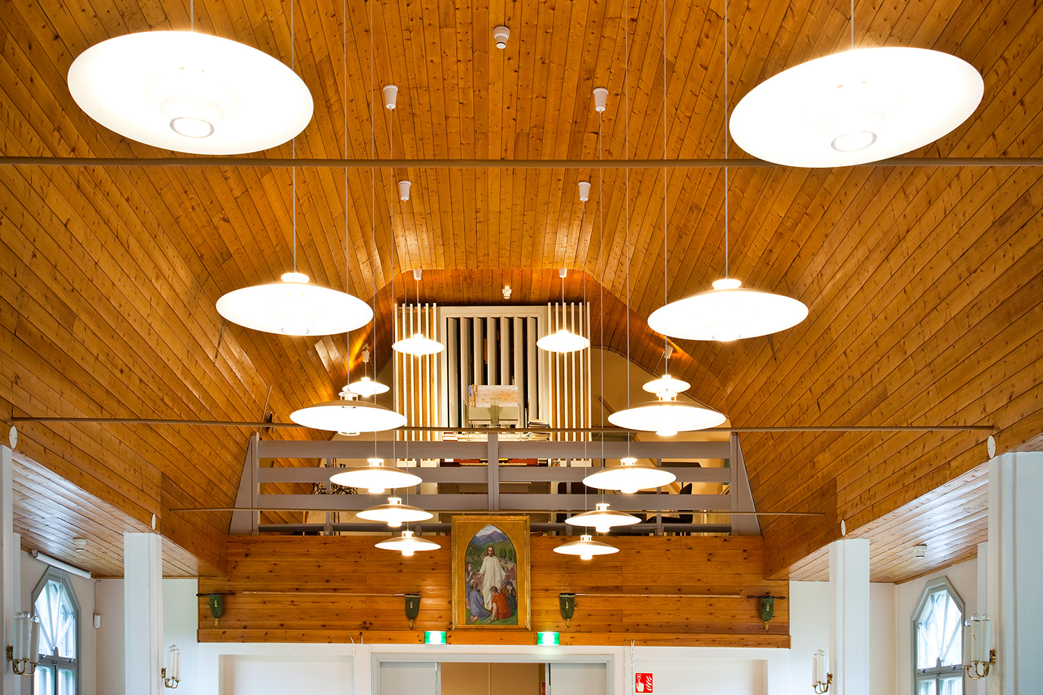 perkkaan kappelin kaareutuva puinen lämminsävyinen sisäkatto, josta riippuu valaisimia, taustalla näkyvät urut ja lehteri sekä maalaus "Hyvä paimen"