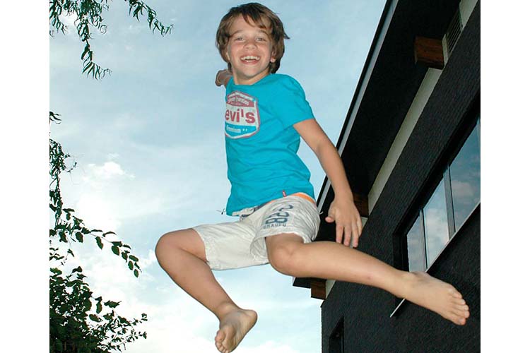 Kuvassa poika hyppää iloisena ilmaan, taustalla sininen iltataivas ja oikealla talo.