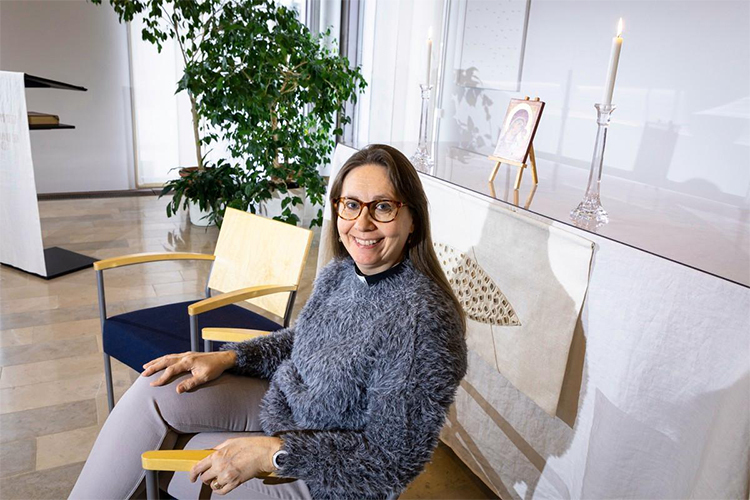 kuvassa pastori Kirsi Muurimäki istu Kalajärven kappelin modernisti kalustetussa aulassa ja hymyilee
