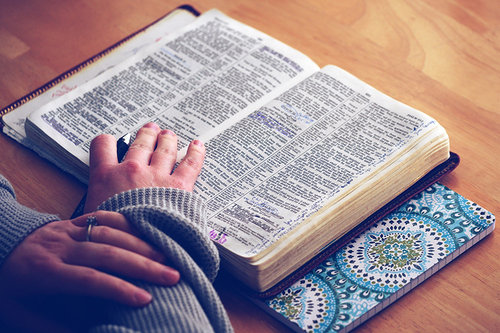 Kuvassa Raamattu ja sitä lukevan henkilön kädet.