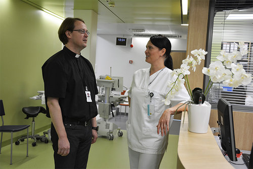 Sairaalapappi keskustelemassa hoitajan kanssa osaston käytävällä.