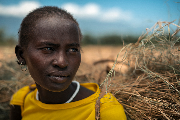 Kenialainen nuori nainen keltaisessa paidassa, kantaa selässään rehua.