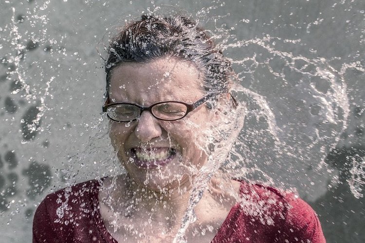 Hymyilevän naisen kasvoille roiskuu vettä.