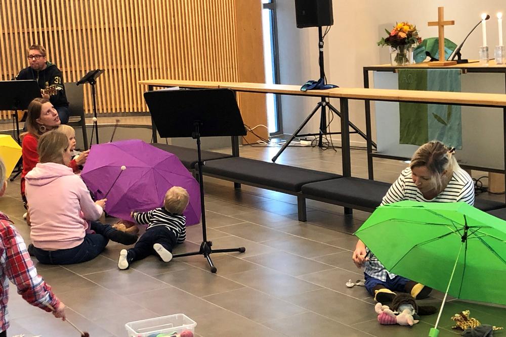 perhemessu Kauklahden kappelissa 2019. Kuvassa lapsia, värikkäitä sateenvarjoja ja vanhempia, alttari oikealla