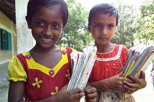 Kaksi tyttöä koulun pihalla kouluvihot käsissään.