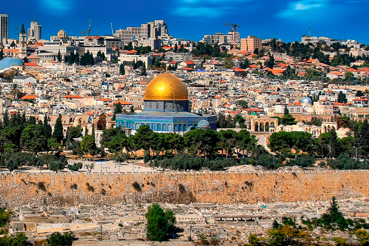 Kuva Jerusalemin kaupungista. Kuvassa paljon kivestä rakennettuja matalia taloja ja taustalla korkeita kerrostaloja sekä nostokurkia, taivas on sininen. Etualalla kultakupolinen kirkko