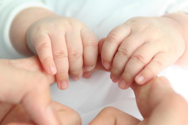 Kuvassa vauvan kädet pitävät kiinni vanhemman sormista.
