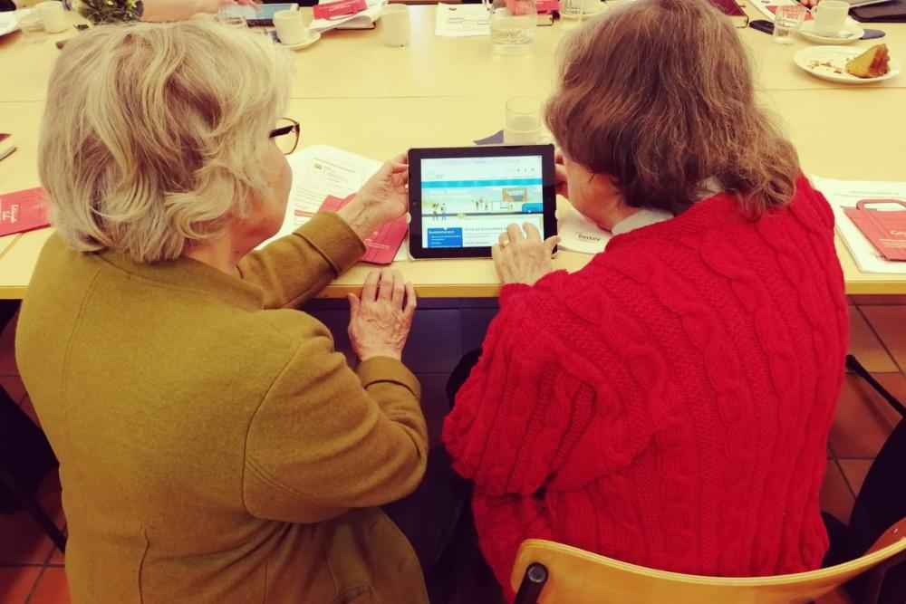 Kuvassa kaksi ikäihmistä opettelvat yhdessä tabletin käyttöä.