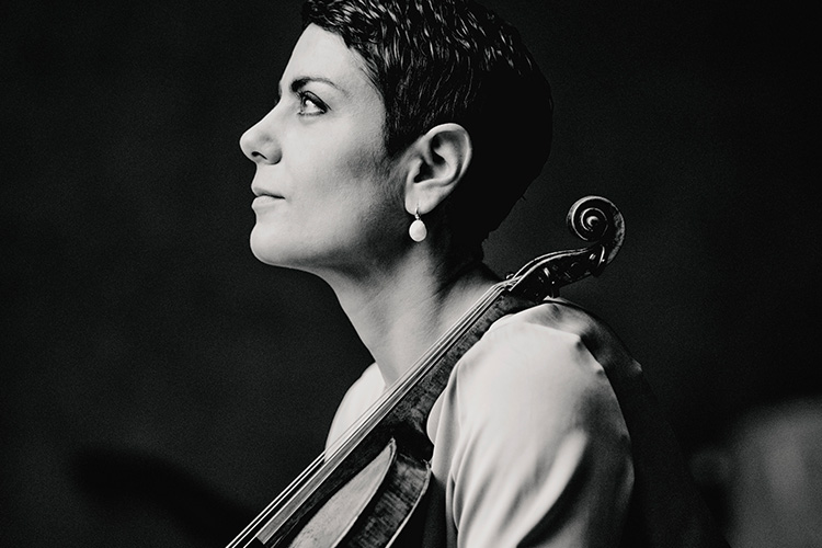 Mustavalkoinen kuva, jossa tummatukkainen nainen nojaa viuluun ja katsoo vasemmalle.