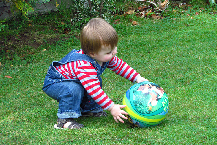 Lapsi leikkii pallolla nurmikolla.