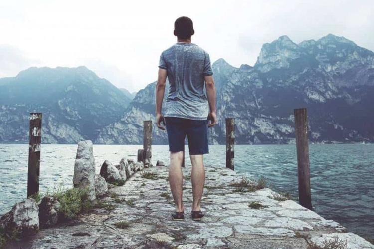 Kuvituksessa mies seisoo laiturilla ja katsoo veden yli vuoria.