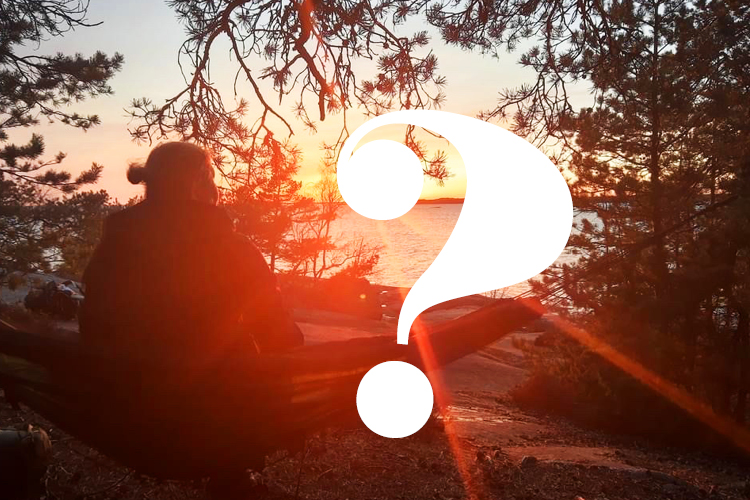 Nainen katsoo kalliolla riippukeinussa auringonlaskuun. Kuvan päälllä on kysymysmerkki.