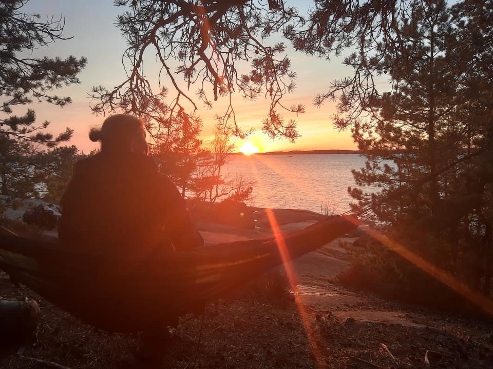 Johdantokurssi kristilliseen meditaatioon Nainen istuu mietiskelemässä kallioisella rannalla auringonlaskun aikaan.