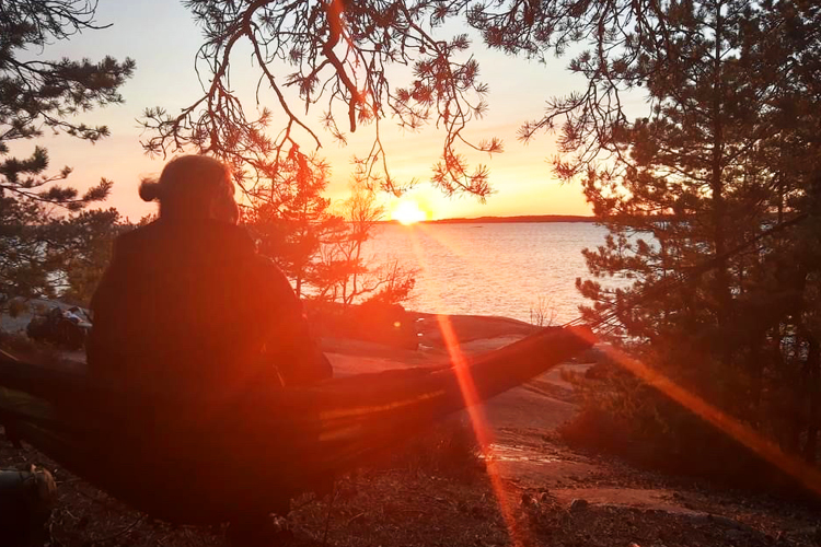 Nainen katsoo kalliolla auringon laskuun.
