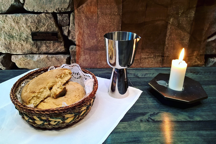 Kuvassa alttaripöydällä kynttilä, leipää korissa ja viinimalja