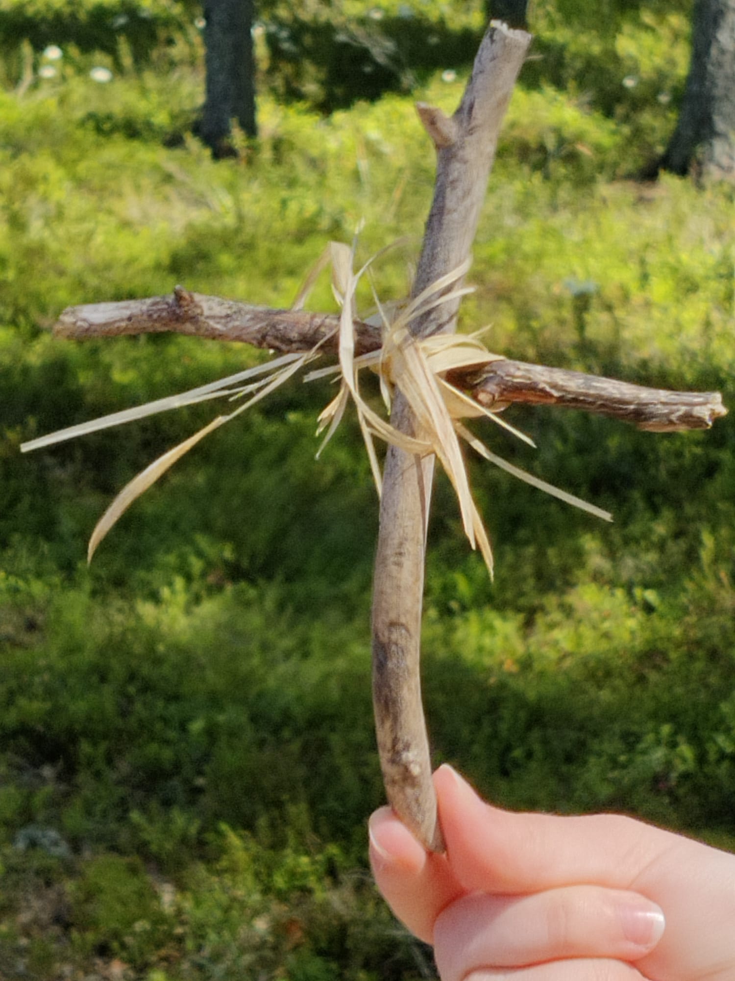 tikuista tehty risti, joka on sidottu heinällä. tautalla mustikkamättäitä