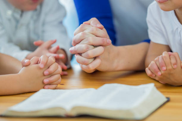 pöydällä avoin Raamattu ja neljät rukoilevat kädet