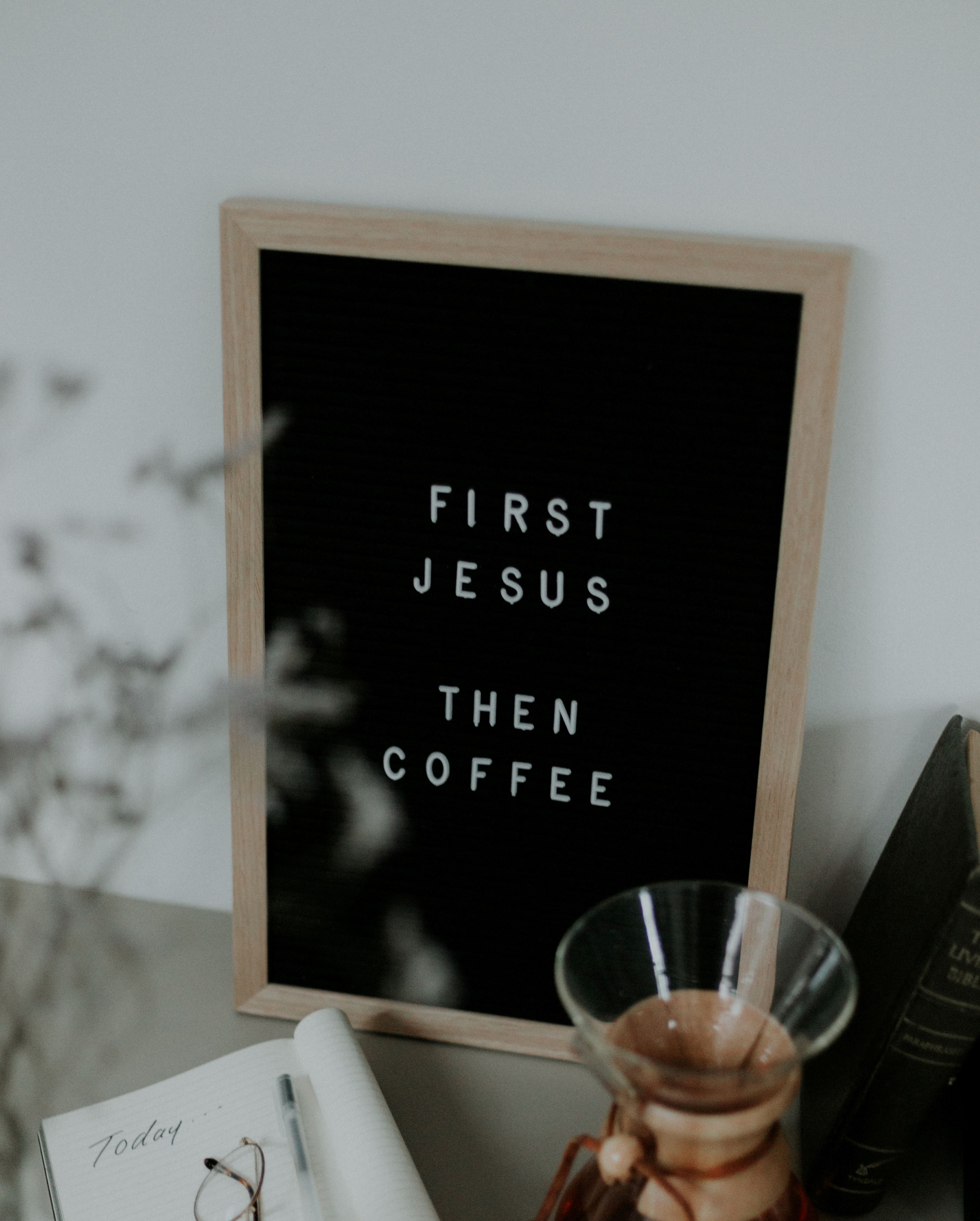 Taulu jossa teksti First Jesus then coffee. Kahvikuppi ja muistikirja vieressä, jossa teksti Today