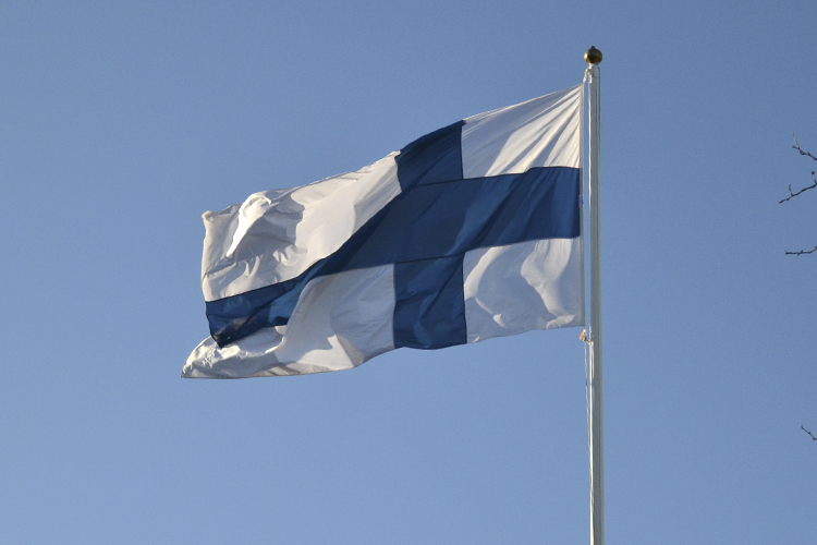 Suomen lippu liehuu sinisellä taivaalla auringossa.