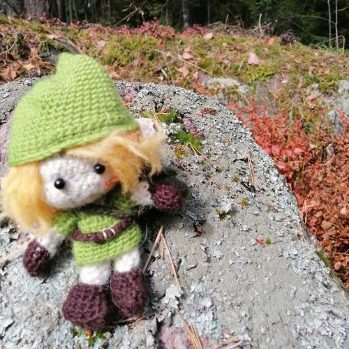 Metsäperhekerho Neulanen-niminen pehmoleluhahmo istuu luonnossa, metsän helmassa.