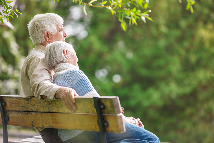 Vanha mies ja nainen istuvat puiston penkillä.