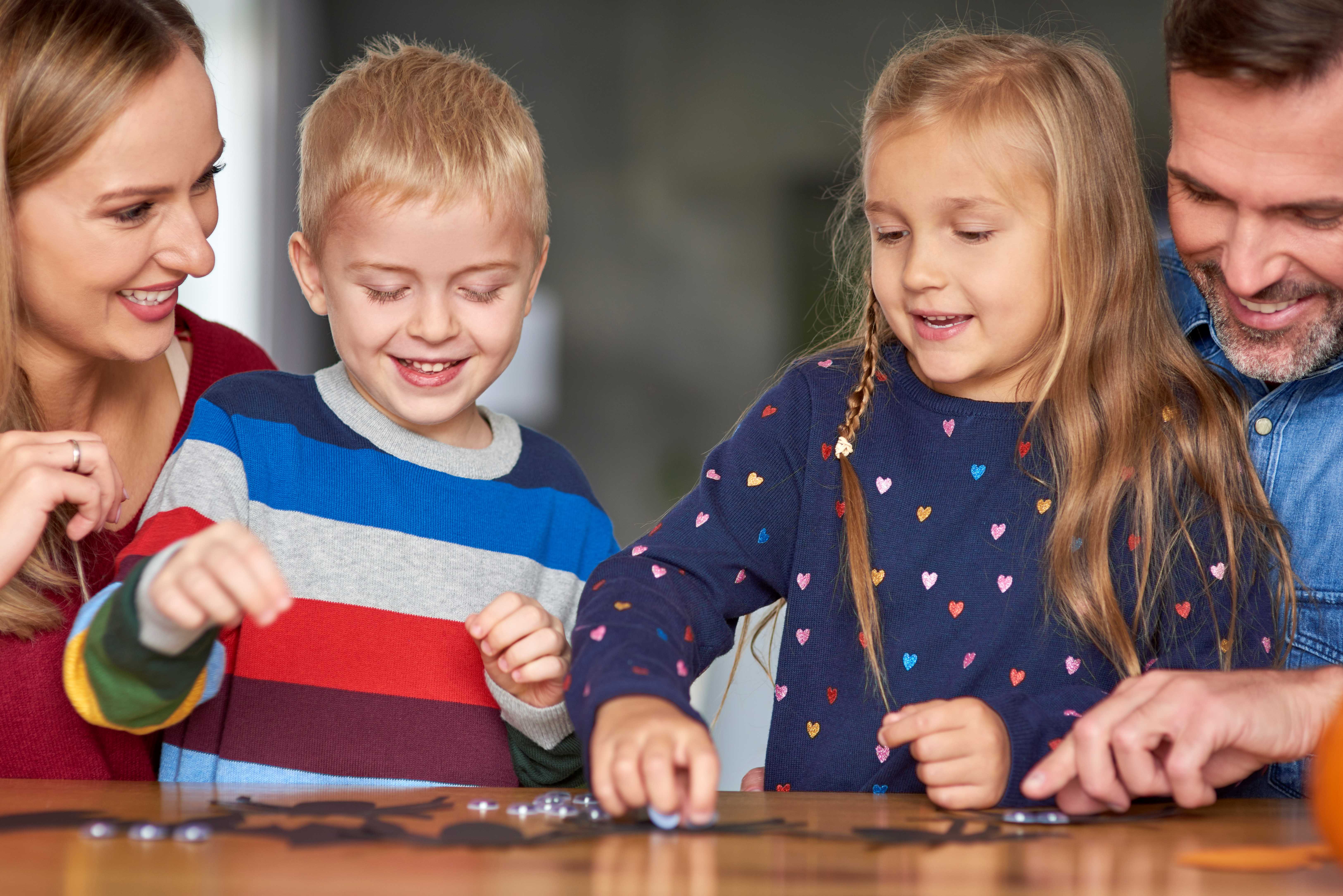 Kaksi aikuista ja kaksi lasta pelaa iloisena lautapeliä.