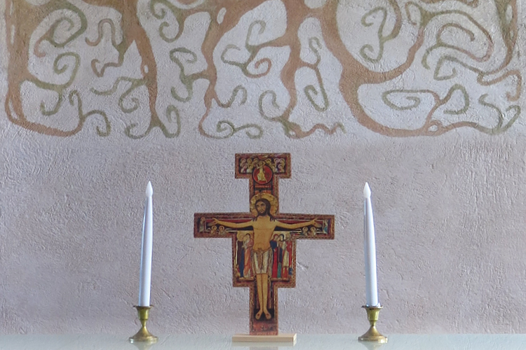 Puinen ikoniristi ja kynttilät rapattua seinää vasten. 