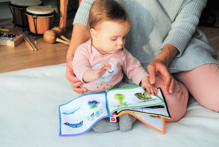 Vauva lukee äitinsä vieressä pehmokirjaa.