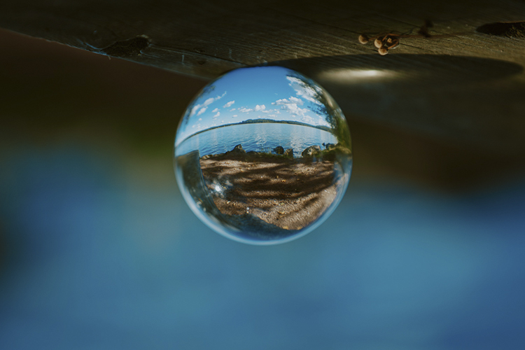 Lasipallosta peilautuu näkymä syyskesäiselle Vitträsk-järvelle. Sinisellä taivaalla on pilviä. Kuva: Aada H...