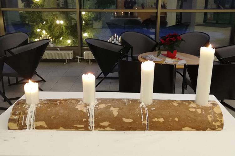 Kuvassa on puinen kynttilänjalka, jossa palaa neljä adventtikynttilää.