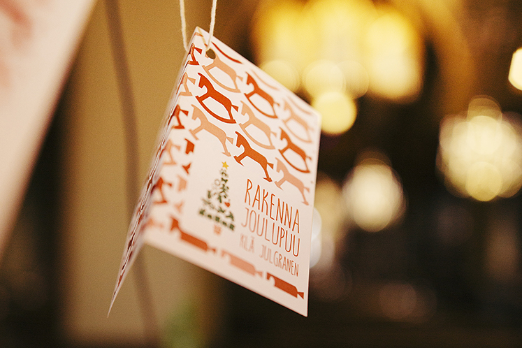 Rakenna joulupuu -kortti on ripustettu kuuseen. Kirkossa on tunnelmallinen valaistus.